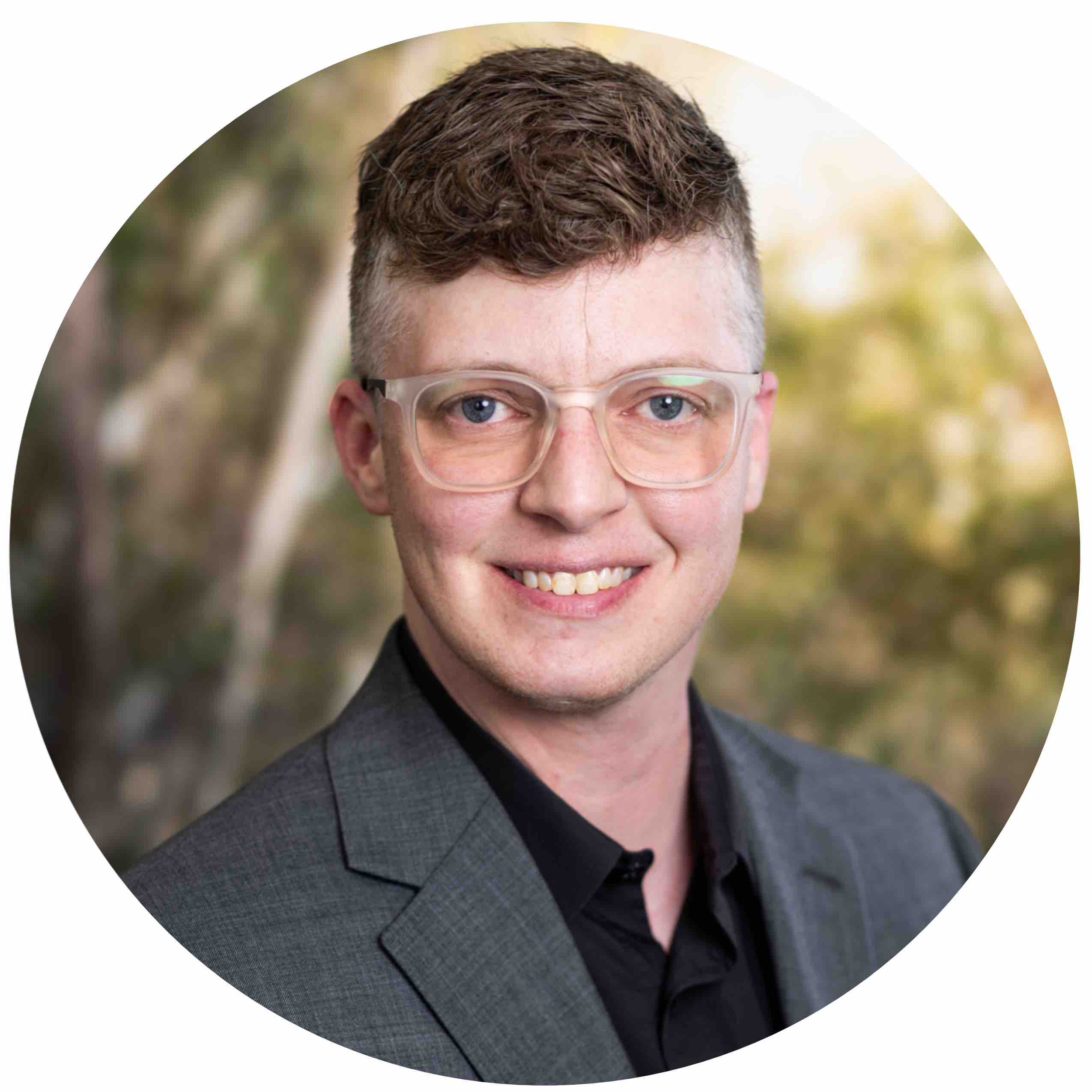 Harper Strickland - headshot of a white adult with short hair, glasses, black shirt and gray suit jacket